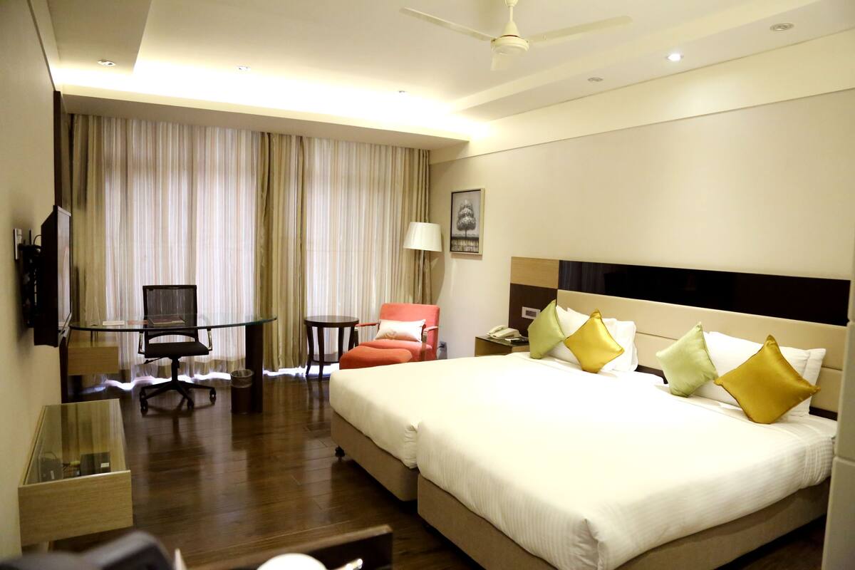A hotel room with a bed, a desk, a chair, a TV, and a ceiling fan.