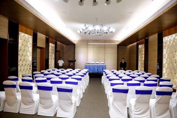 A conference room with rows of white chairs with blue sashes, a podium, and a chandelier.