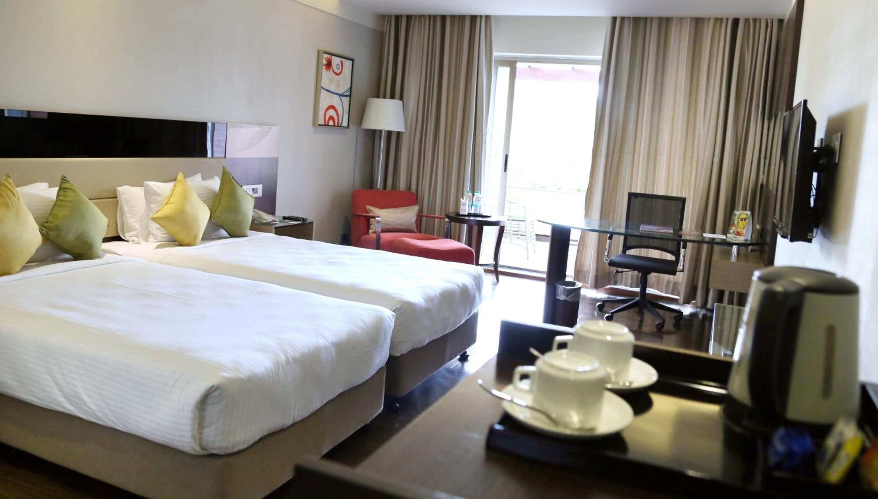 Habitación de hotel con dos camas, un escritorio con silla, televisión y ventana con cortinas.