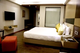 Habitación de hotel con una cama grande, un televisor montado en la pared, un escritorio con teléfono y una ventana con persianas.
