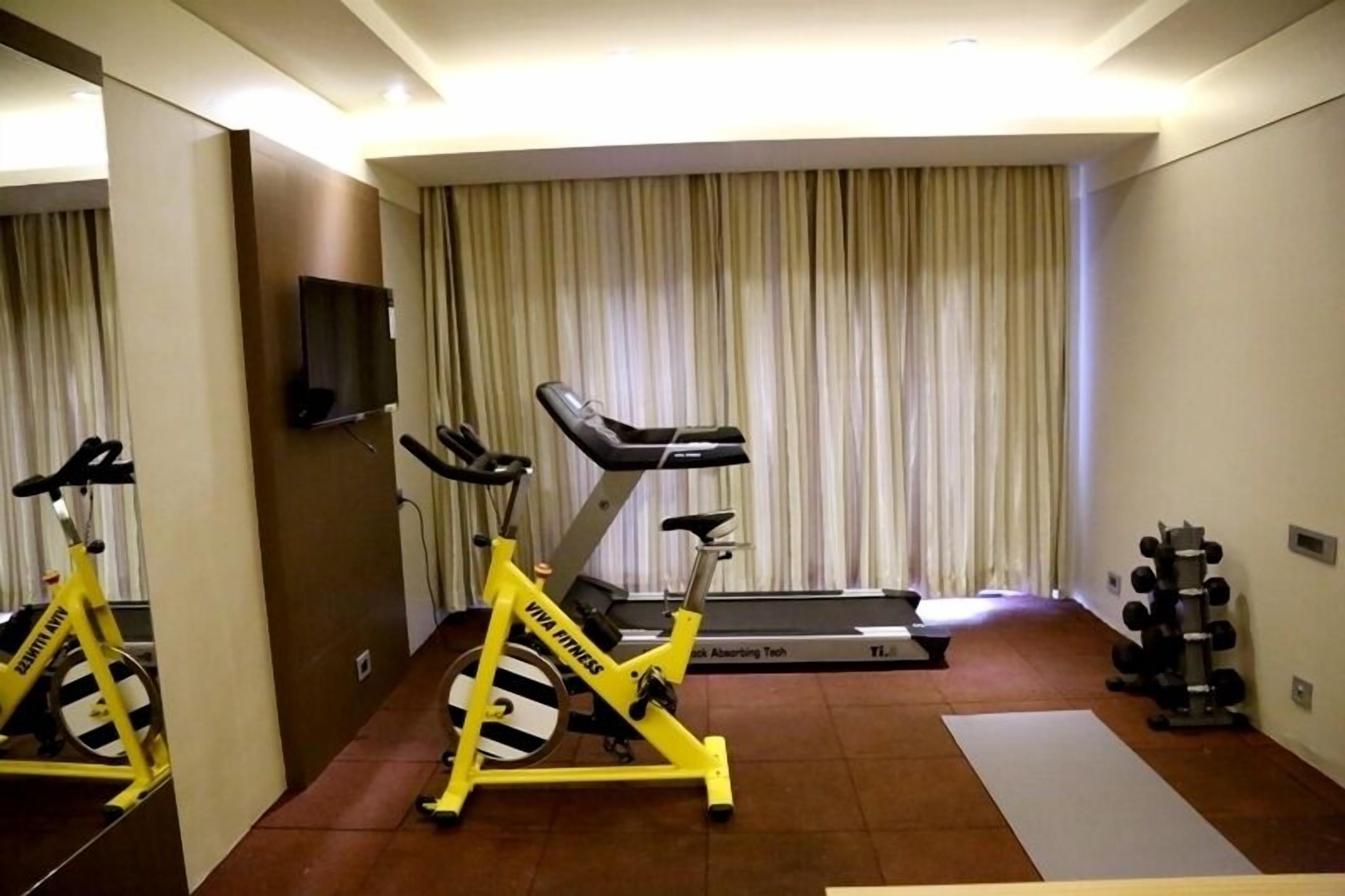 Une salle de sport compacte équipée d’un vélo d’appartement, d’un tapis de course et d’un ensemble d’haltères.
