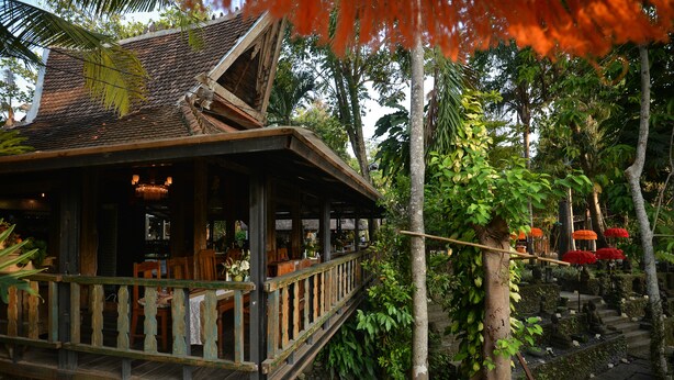 A wooden structure with a balcony, surrounded by lush greenery and a stone pathway. - Taman Nauli Bed & Breakfast (Tibubeneng)