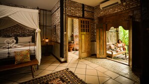 A bedroom with a four-poster bed, a bench, and a patterned rug. - Taman Nauli Bed & Breakfast (Tibubeneng)