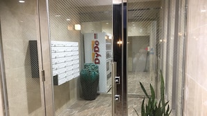 A modern hotel lobby with a glass door entrance, a reception desk, a large decorative vase, and a potted plant. - Chura Gahna House Tsubogawa Naha (Naha)
