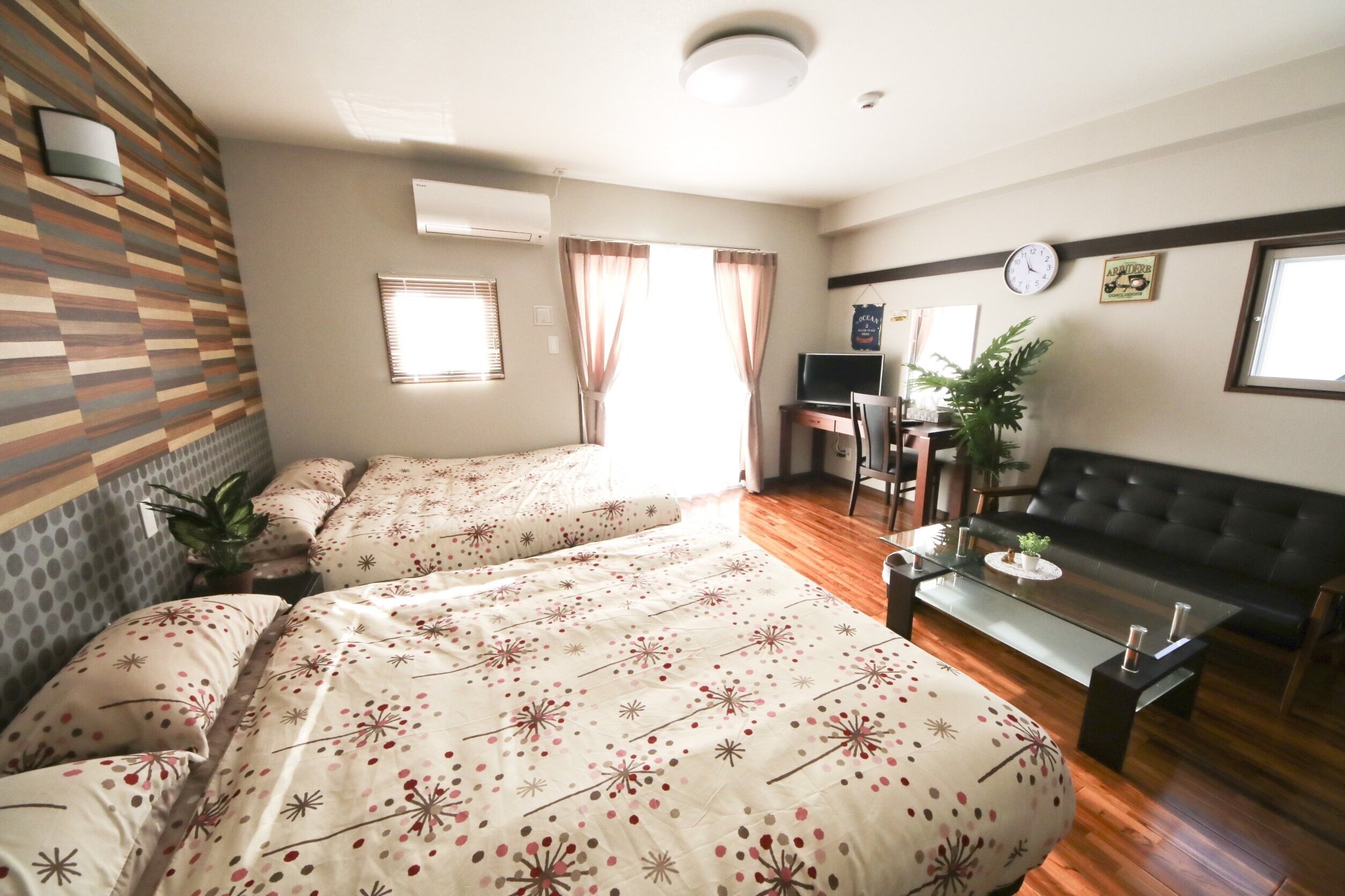 A hotel room with two beds, a sofa, a TV, and a desk.