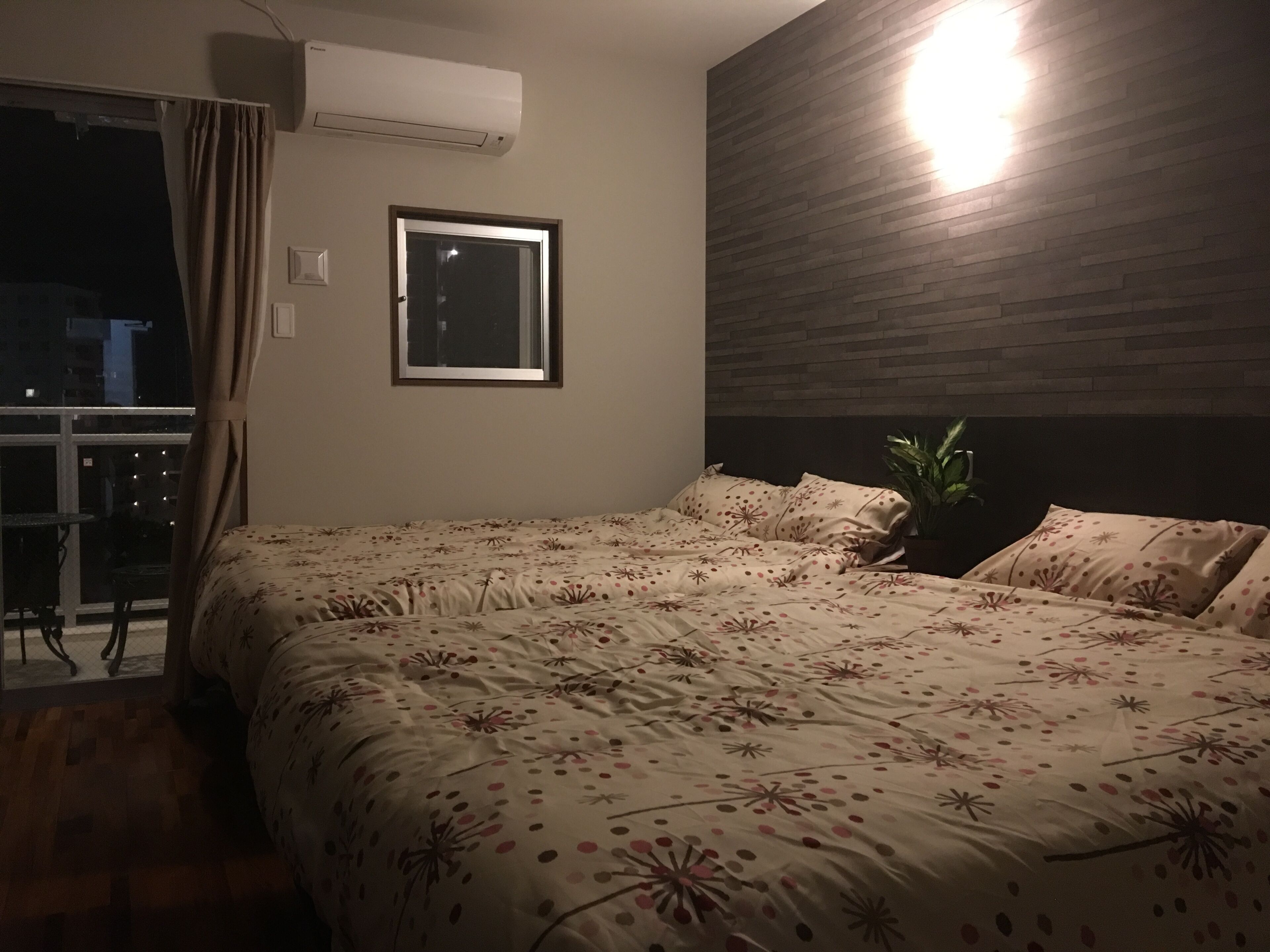 Un dormitorio con una cama grande, un equipo de aire acondicionado, una ventana y una planta en maceta.