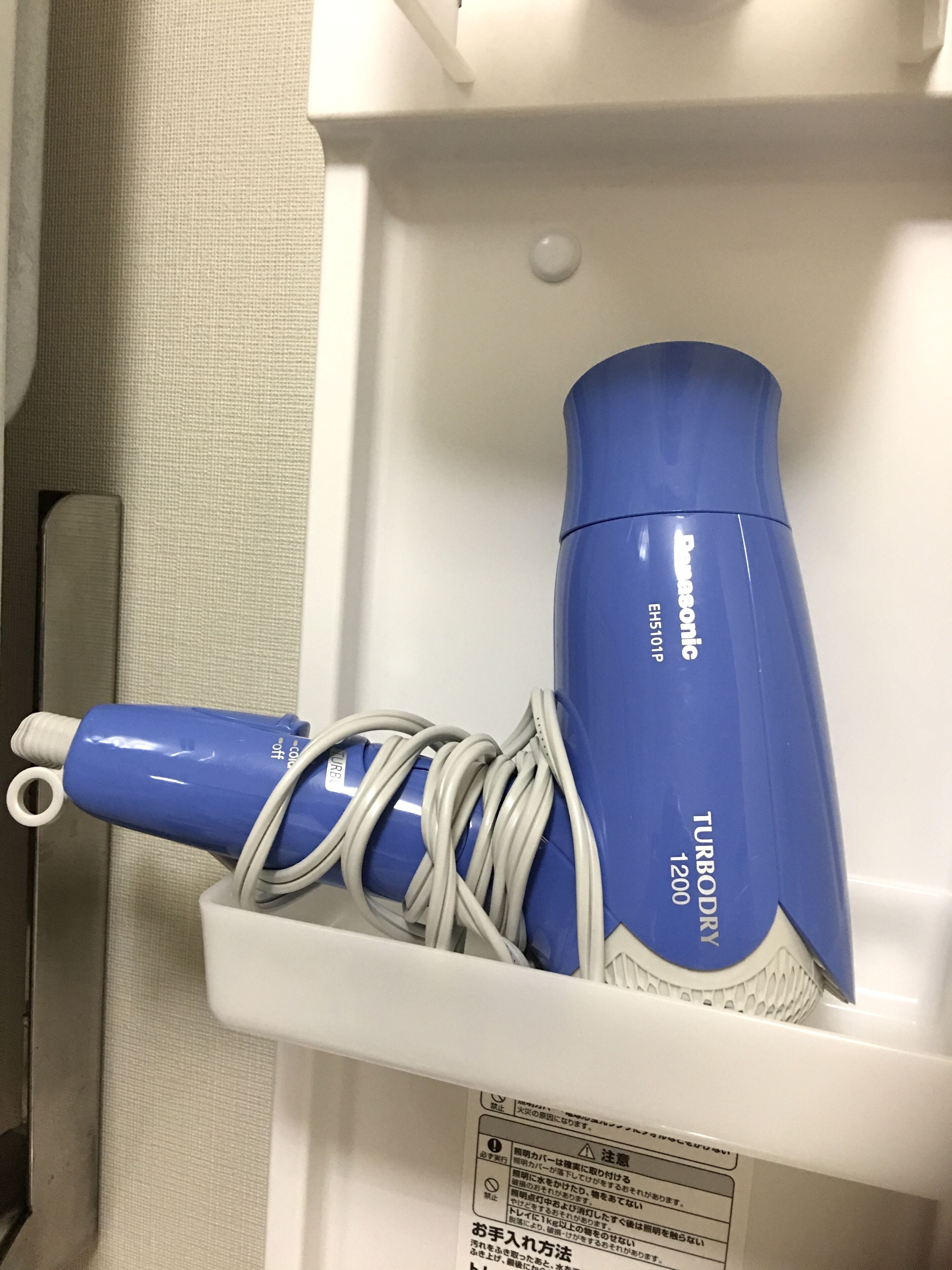 A blue hairdryer and its charging cable coiled in a white drawer.