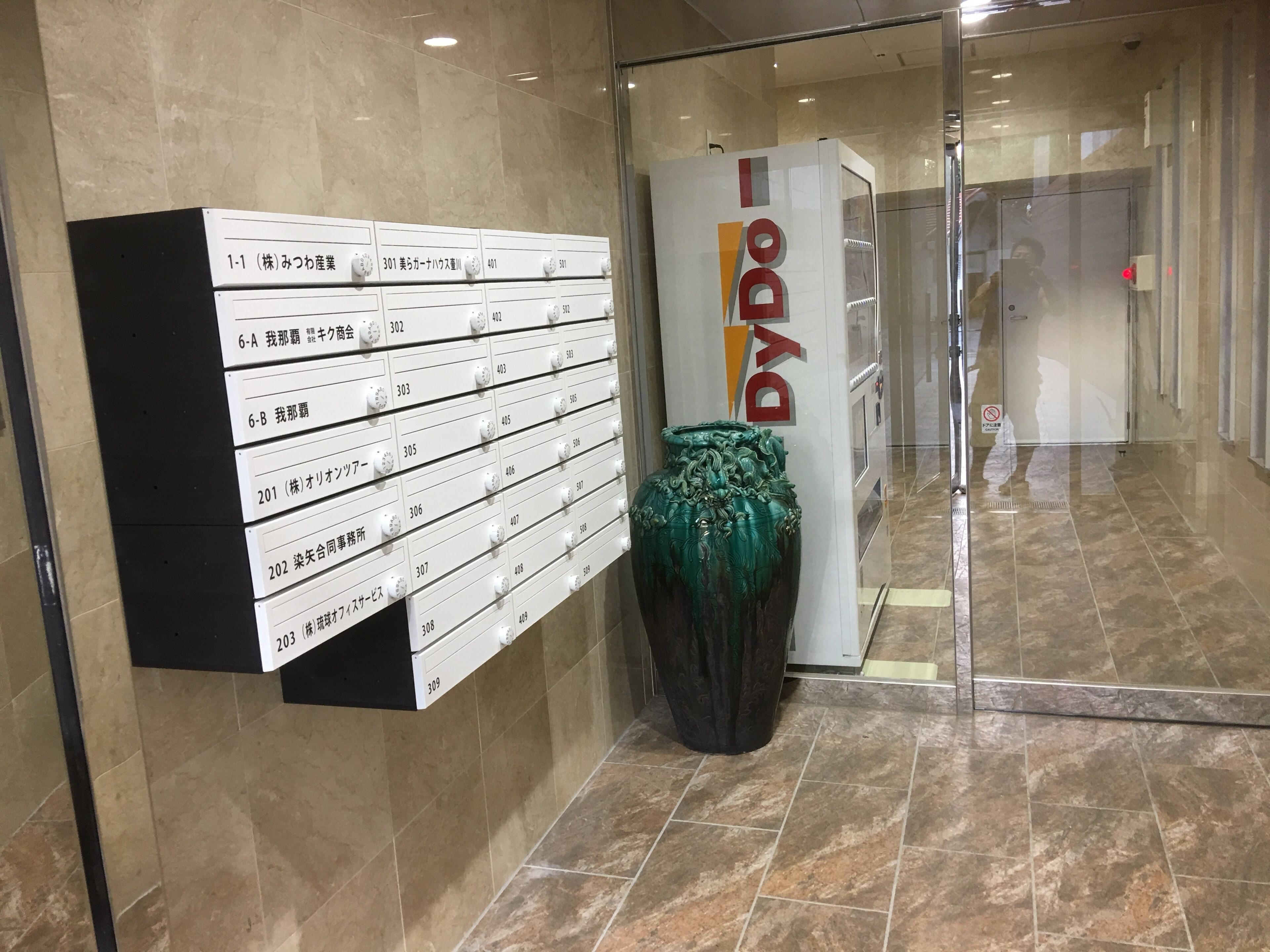 Recepção de hotel com um diretório fixado na parede contendo números de quartos e um vaso grande.