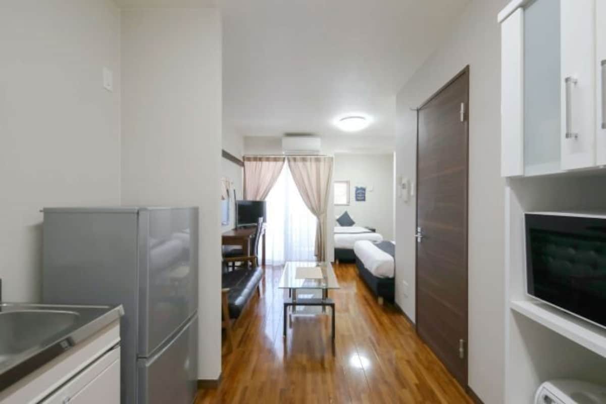 Una habitación de hotel compacta con kitchenette, una cama, una mesita y un televisor.