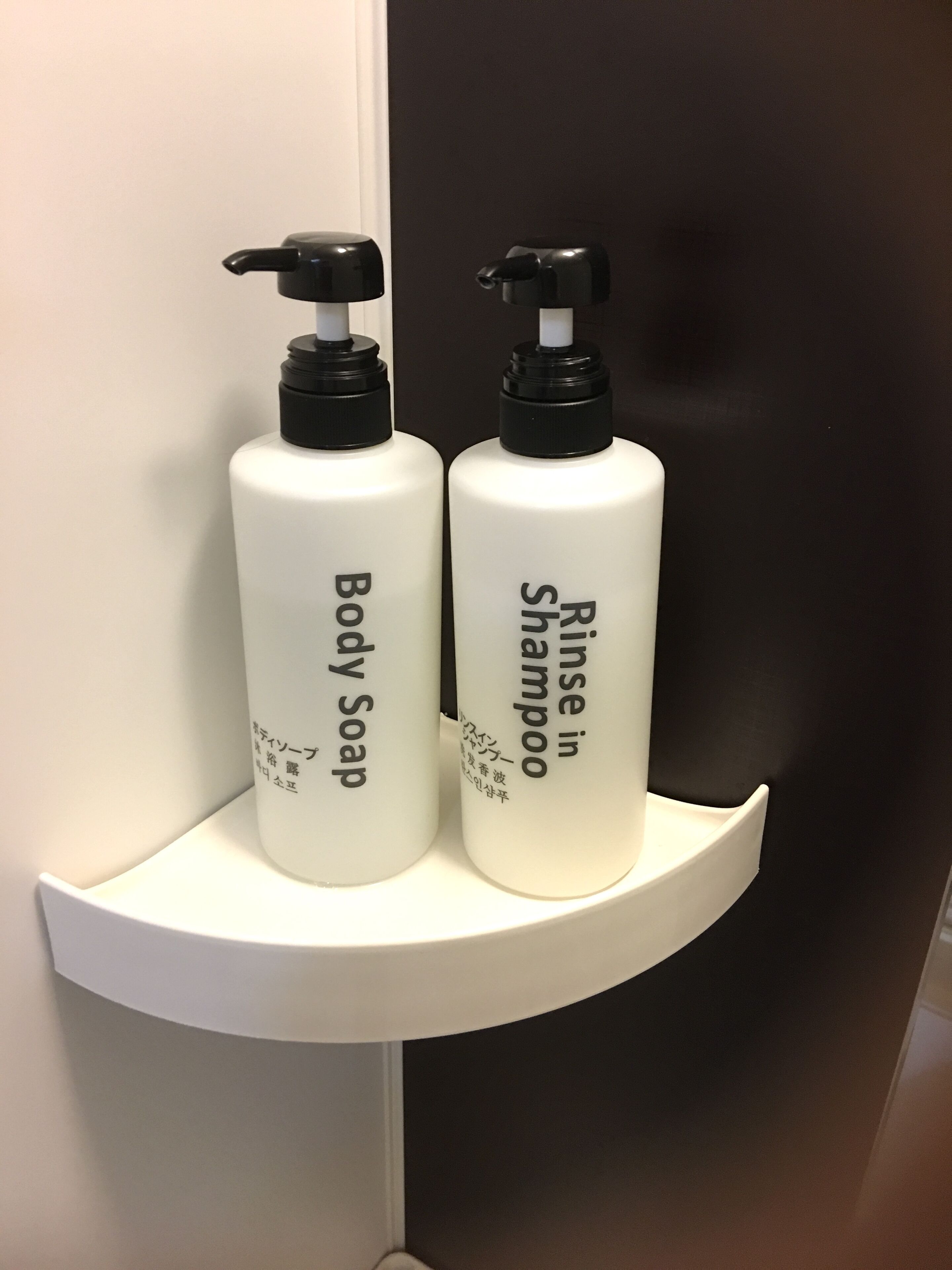 Dos botellas de jabón corporal y un envase de acondicionador sobre un estante blanco.