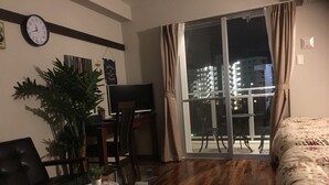 A modern living room with a glass dining table, a sofa, a TV, and a balcony with a city view. - Chura Gahna House Tsubogawa Naha (Naha)