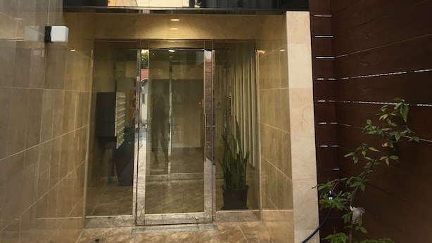A building entrance with a glass door, a wooden ceiling, and a sign with Japanese characters. - Chura Gahna House Tsubogawa Naha (Naha)