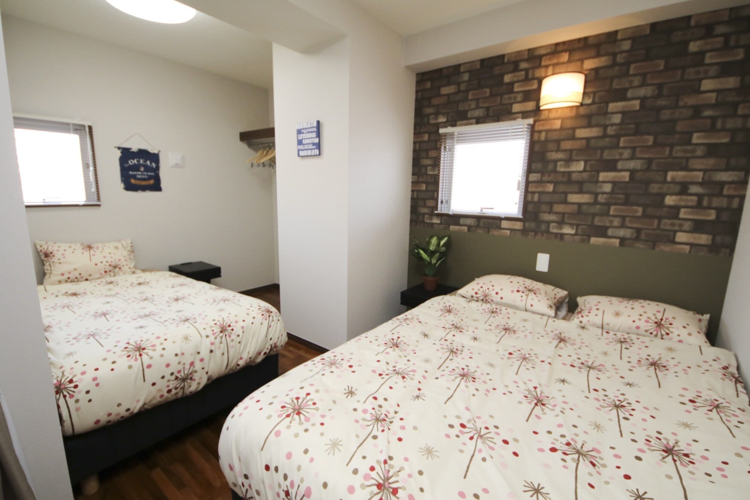 A bedroom with two beds, a brick accent wall, a potted plant, and a sign on the wall.