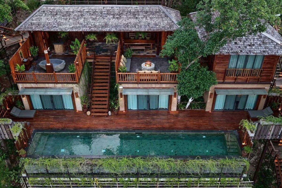 Une maison en bois à deux étages, dotée d’une piscine, d’une terrasse en bois et d’un espace salon extérieur.