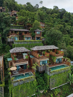 A multi-story wooden building with balconies, a swimming pool, and lush greenery surrounding it.