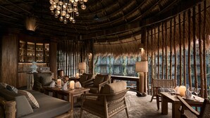 A cozy, rustic room with wicker furniture, a wooden table set for dining, and a large window with a view of a building. - Dinso Resort & Villas Phuket, Vignette Collection by IHG (Patong)