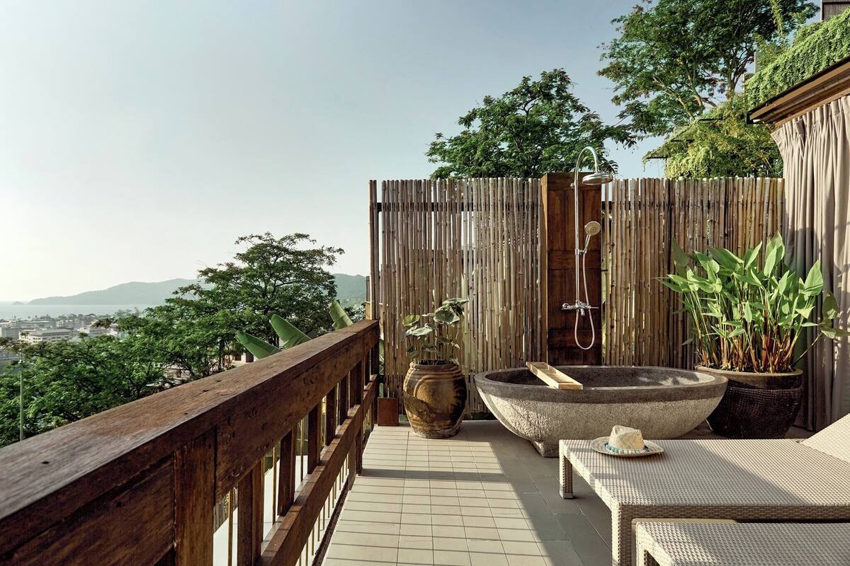 A balcony with a wooden railing, a large stone planter, a potted plant, and a stone bathtub.