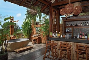 A wooden outdoor bar area with a stone basin, bamboo furniture, and a variety of bottles on shelves. - Dinso Resort & Villas Phuket, Vignette Collection by IHG (Patong)