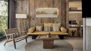 Een moderne woonkamer met een houten wandpaneel, een bank met kussens, een fauteuil, een salontafel en een flatscreen televisie aan de muur.