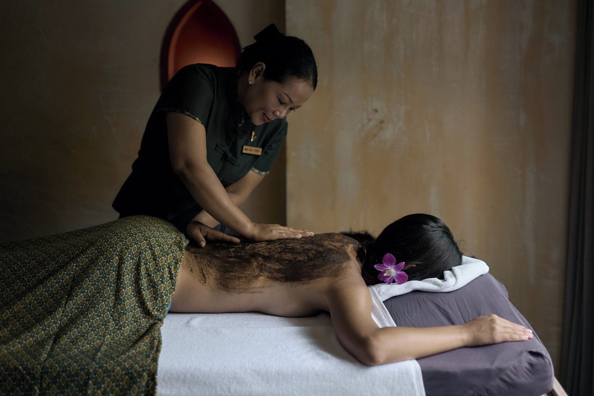 A massage therapy session in a room with a single bed, a towel, and a wall-mounted shelf.