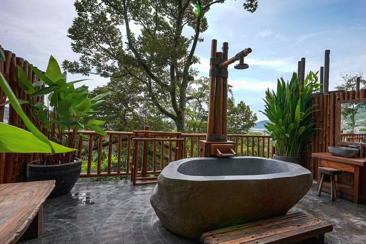 Un espace de détente extérieur comprenant un bassin en pierre, une terrasse en bois, une clôture en bambou et des plantes en pot.