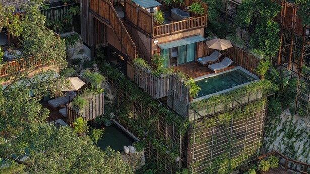 Een houten gebouw met twee verdiepingen, een balkon, een zwembad en weelderige beplanting.