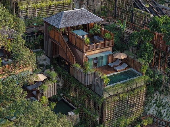 Een houten gebouw met twee verdiepingen, een balkon, een zwembad en weelderige beplanting.