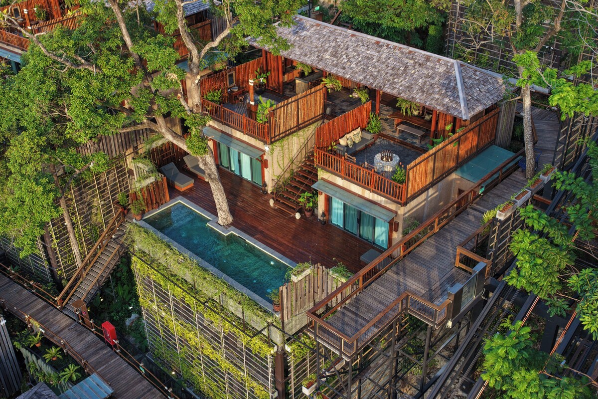 A multi-level wooden house with a swimming pool, outdoor seating, and a fire pit.