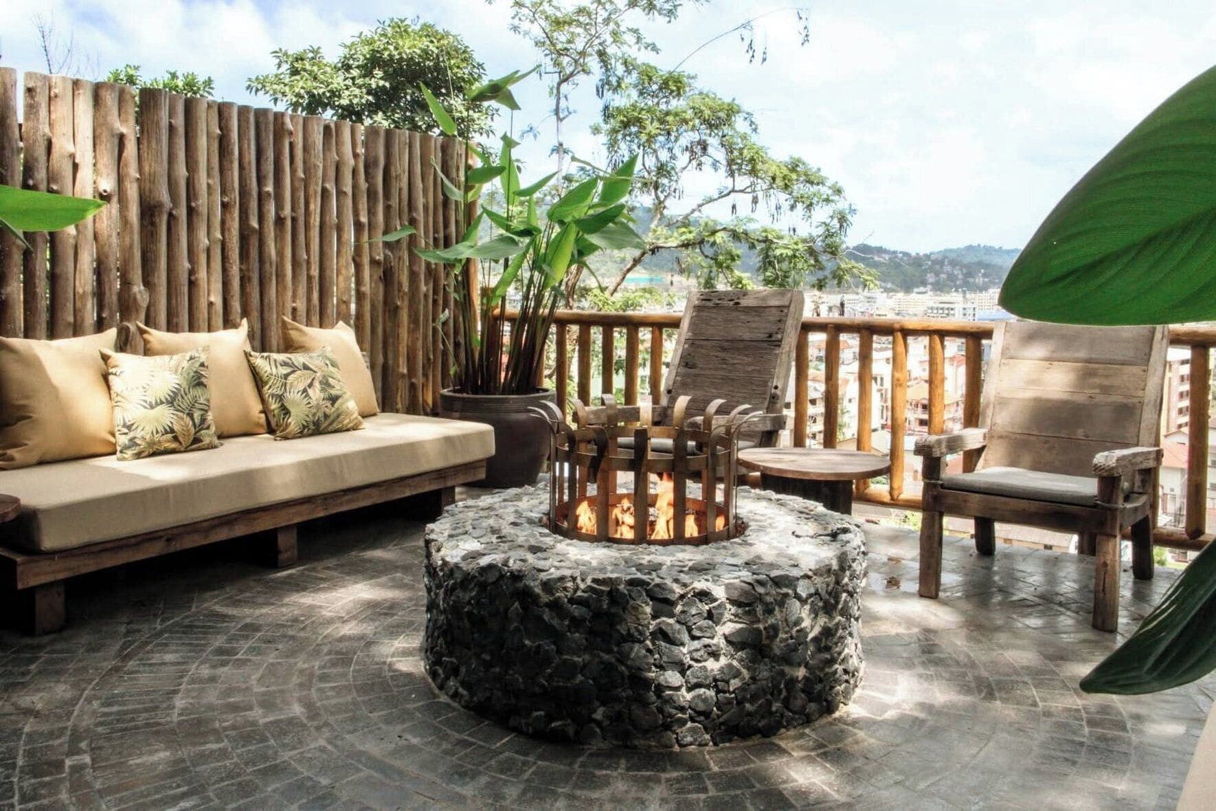 A patio with a stone fire pit, wooden furniture, and a wooden fence.