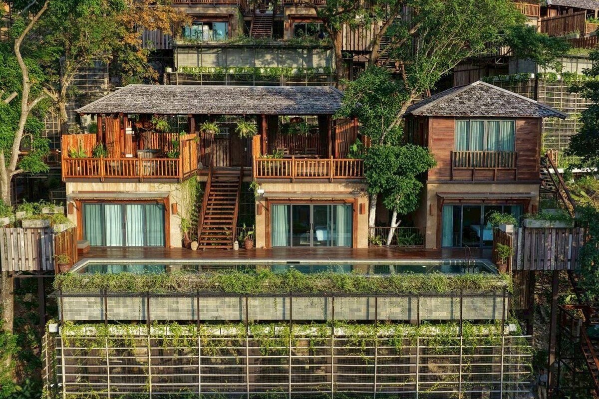 Ein mehrstöckiges Haus mit einem Pool mit Glasboden, Holzbalkonen und einer Treppe, die zu den oberen Stockwerken führt.