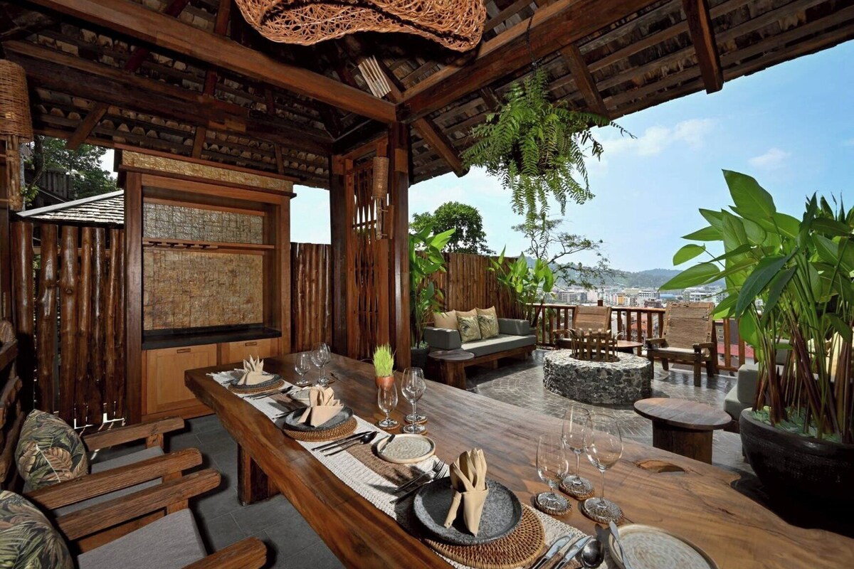 A wooden dining area with a table set for two, a stone fireplace, and a view of the city.
