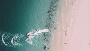 Luchtbeeld van een strand met een boot die een kielzog achterlaat, mensen die zwemmen en een zandstrand.