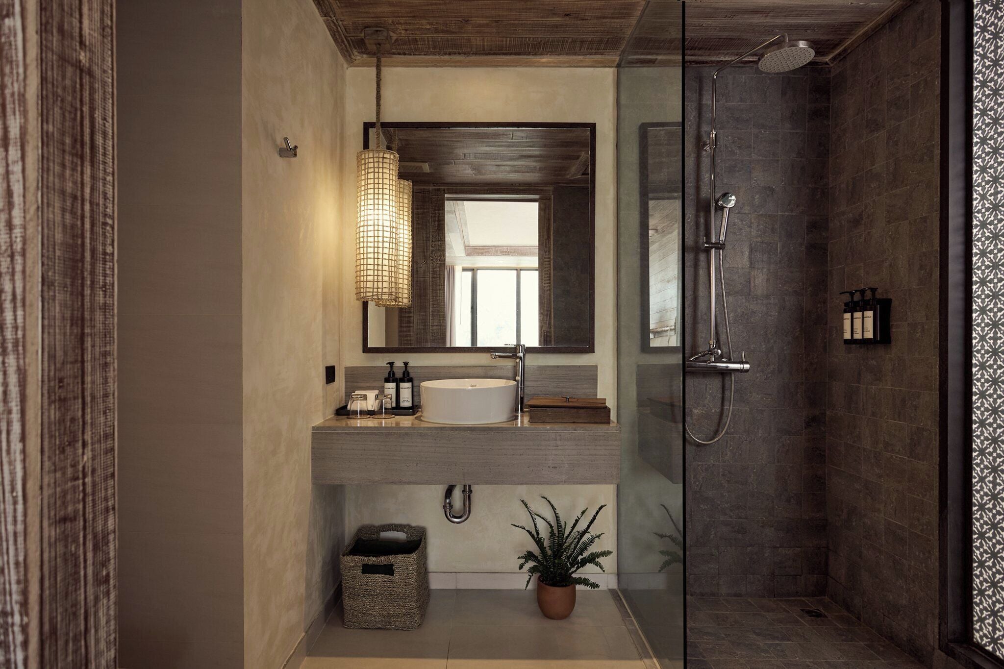A modern bathroom with a large mirror, a round sink, a shower, and a potted plant.