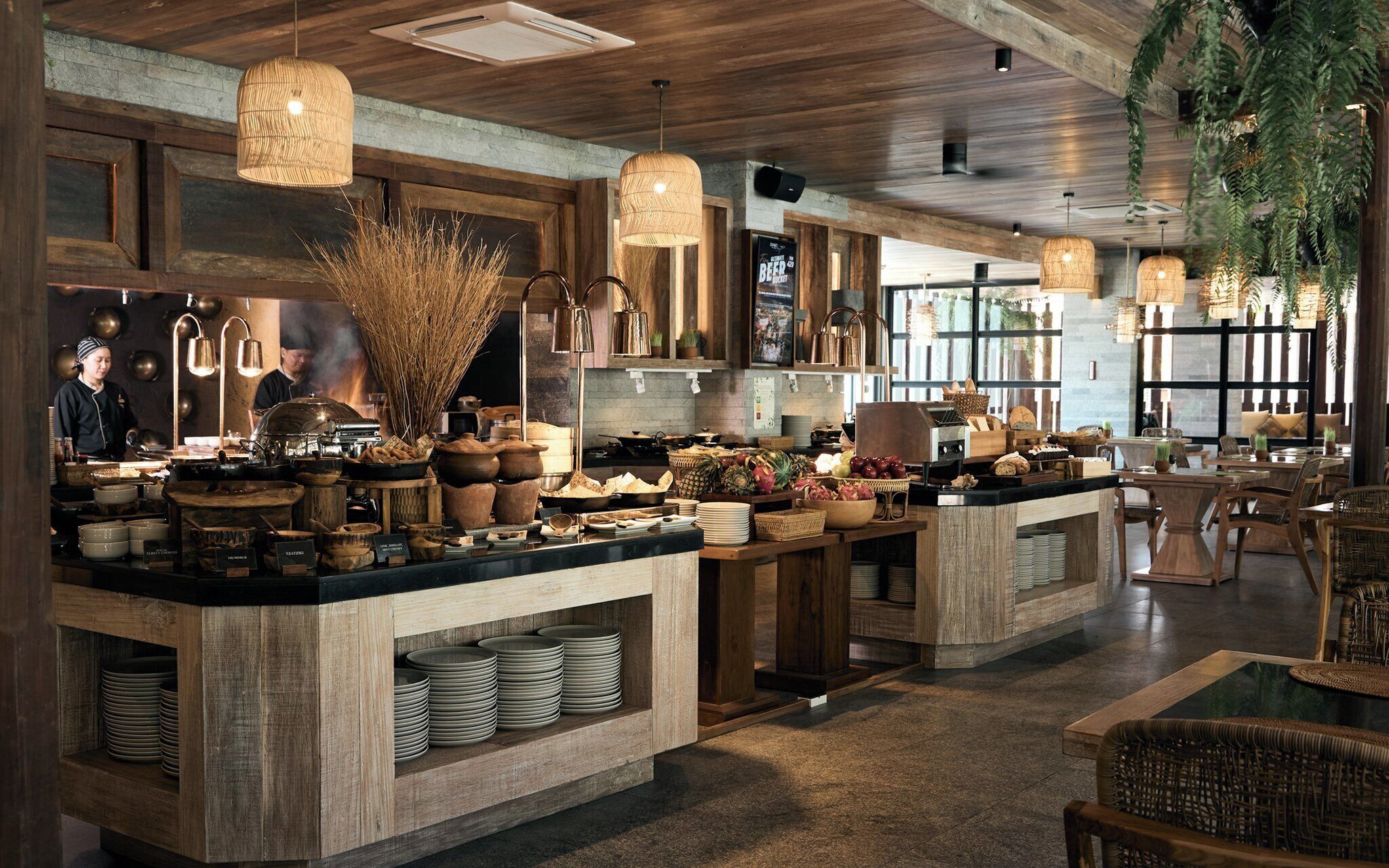 A restaurant with a rustic interior, featuring wooden beams, a central island with food and drink, and hanging baskets.