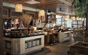 A restaurant with a rustic interior, featuring wooden beams, a central island with food and drink, and hanging baskets.