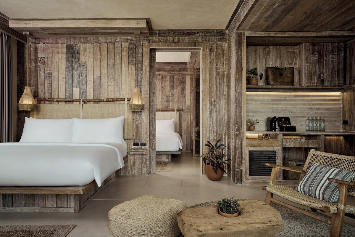 A room with a large bed, a small sofa, a wooden coffee table, and a potted plant.