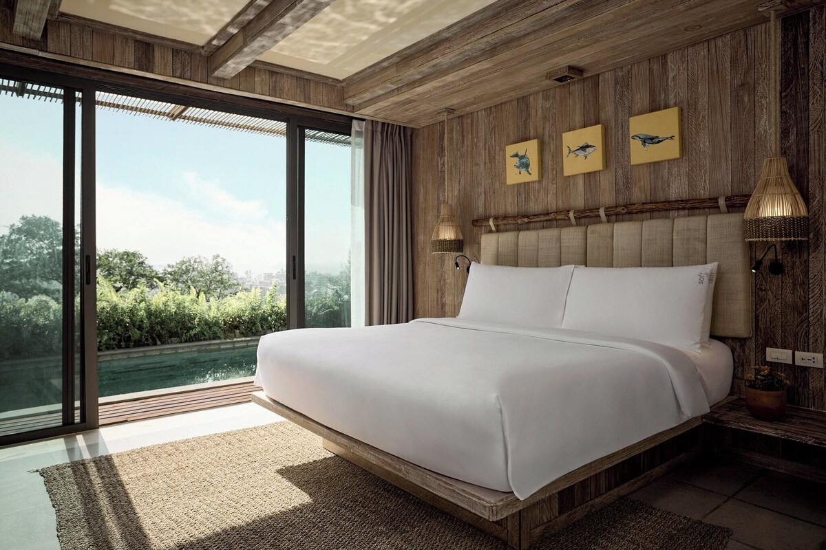 Een slaapkamer met een groot bed, houten wanden en uitzicht op groen.