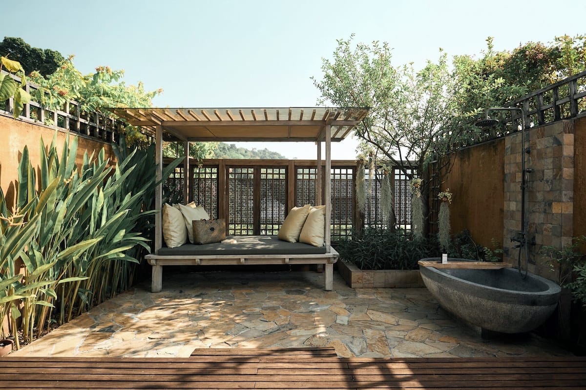 A patio with a wooden bench, a stone bath, and a pergola.