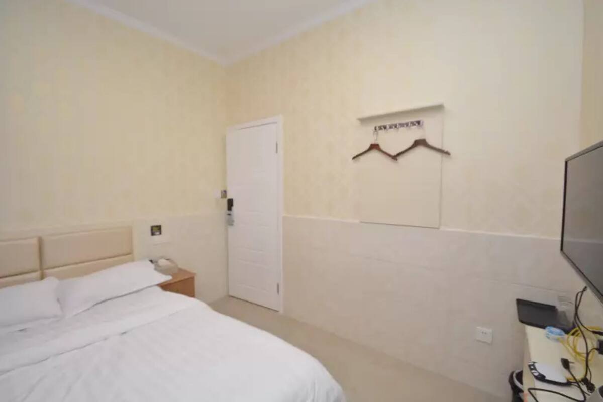 A bedroom with a bed, a bedside table, a door, and a wall-mounted coat rack.