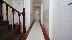 A hallway with a wooden staircase, white walls, and a red-tiled floor. - LuHuai Hotel (Nanjing)