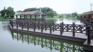 A wooden bridge over a calm body of water with a gazebo structure on the left. - LuHuai Hotel (Nanjing)