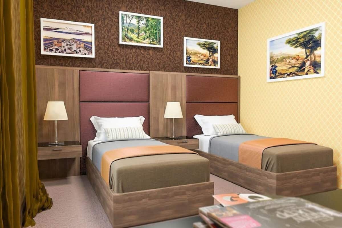 Ett hotellrum med två sängar, trägavlar och tre inramade tavlor på väggen.