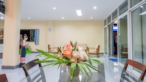 Eine Hotelhalle mit Glastisch, Stühlen, einer floralen Dekoration und einer Rezeption.