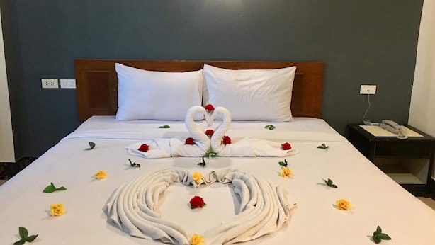 Ein ordentlich bezogenes Bett mit einer Schwan-Handtuch-Arrangement und verstreuten Blumen.