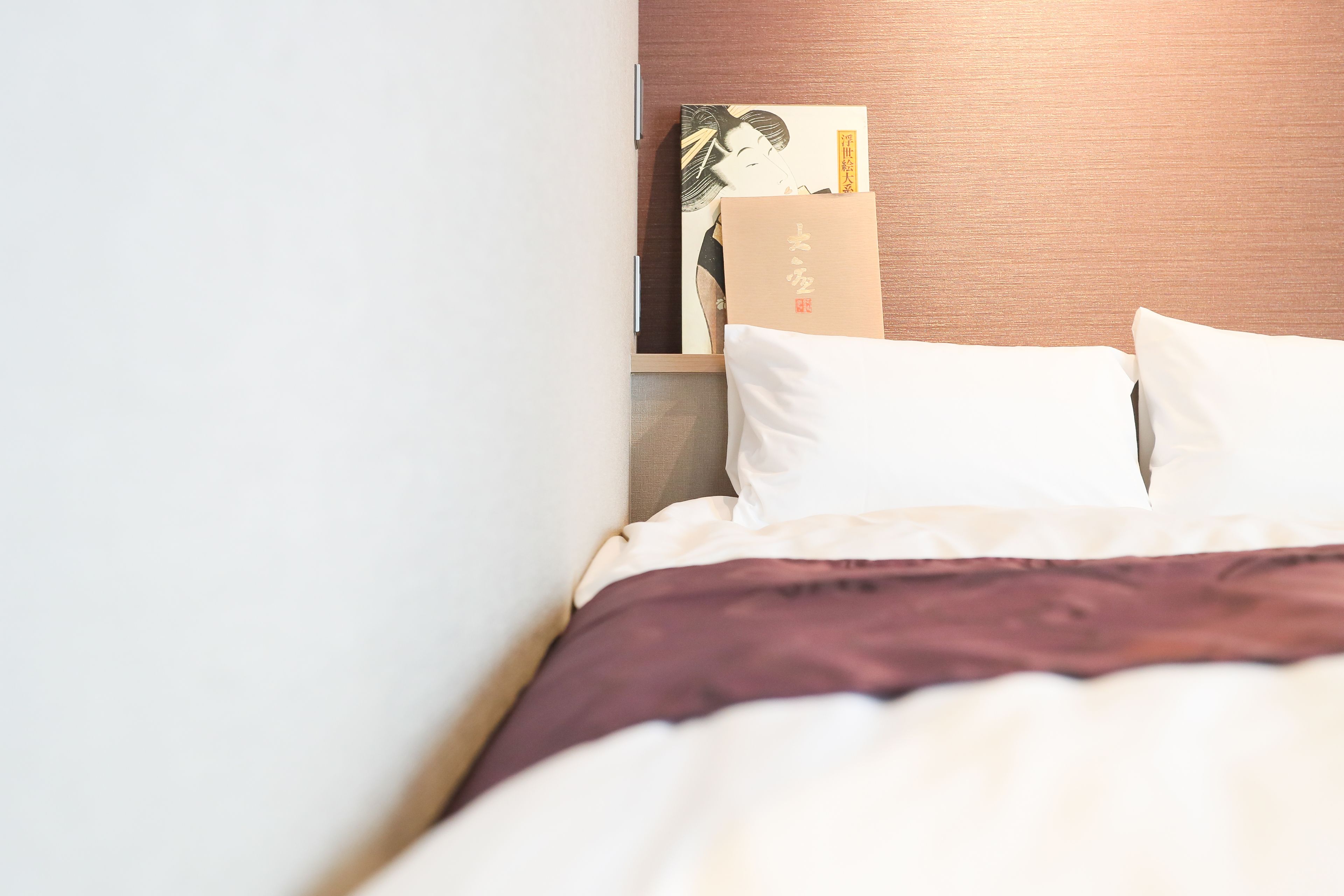 Una cama bien tendida con ropa de cama blanca y marrón, un cabecero de madera y una obra enmarcadas en la pared.