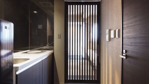 A narrow hallway with a modern design, featuring a kitchen area with a refrigerator and sink, a wooden floor with a striped pattern, and a door with vertical slats.