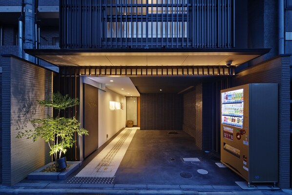 A narrow alleyway with a vending machine on the right and a small tree on the left.
