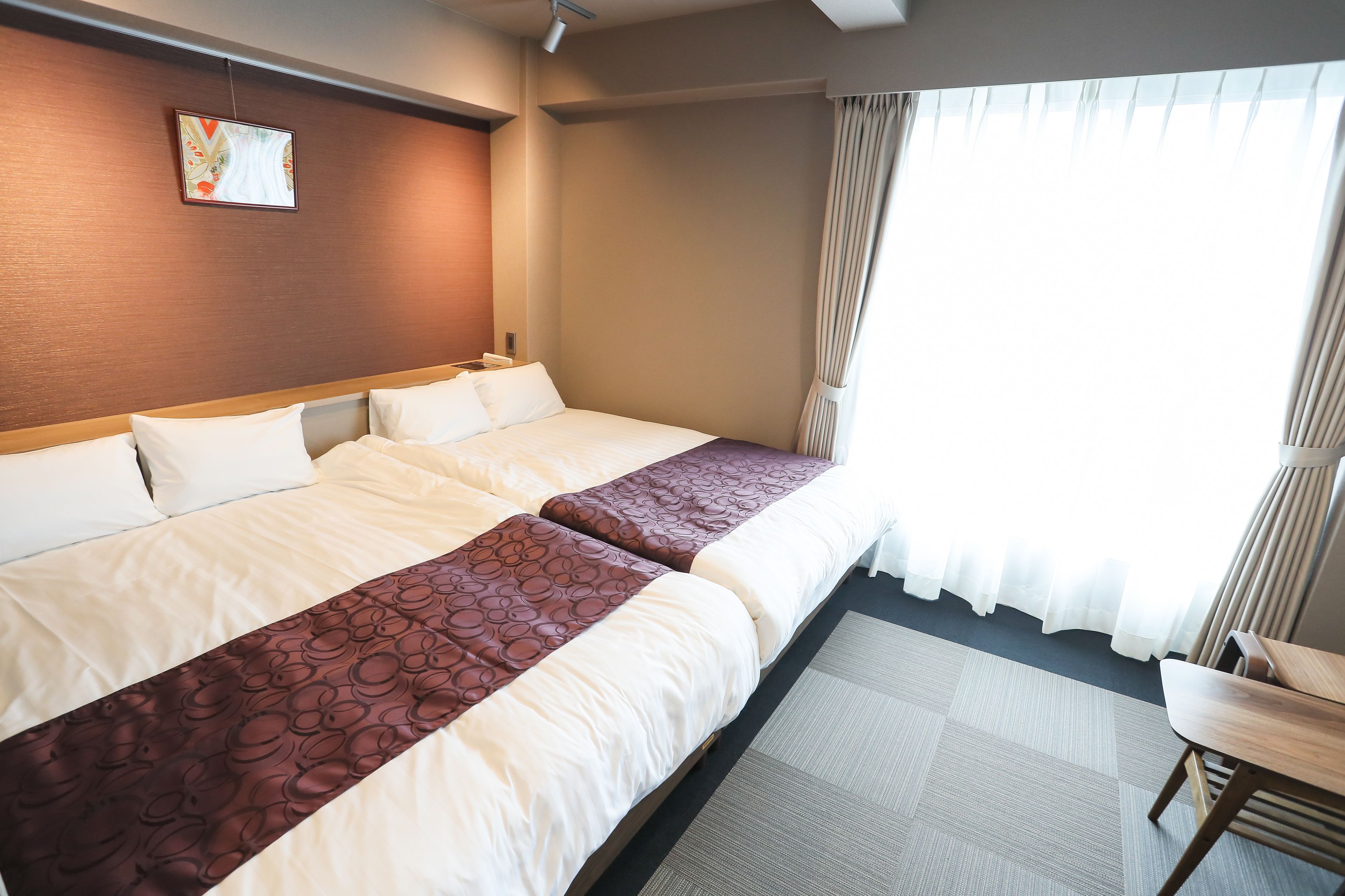 A hotel room with two beds, a wooden headboard, a small table, and a window with curtains.