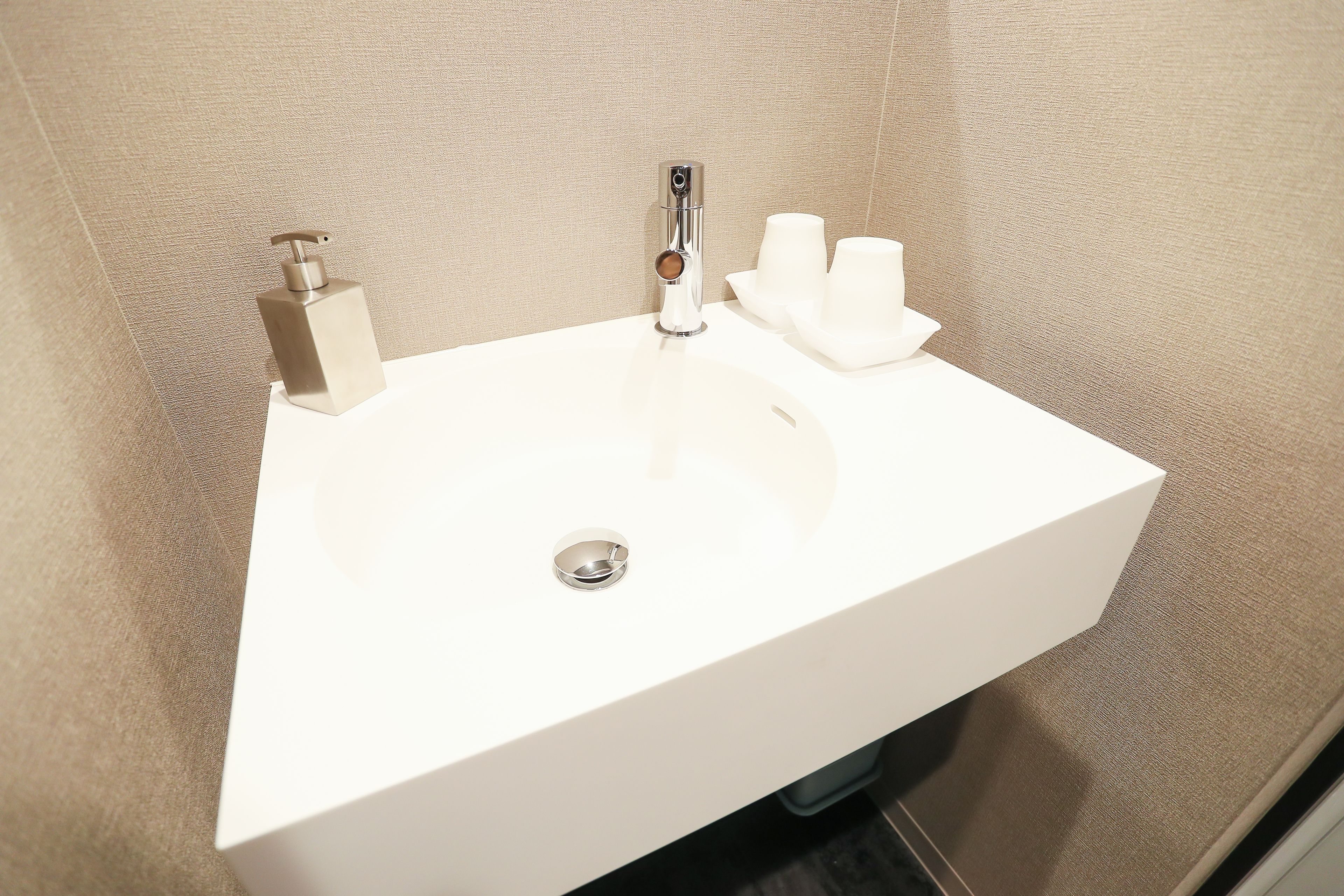 Un lavabo blanc pour la salle de bain, doté d’un robinet chromé, d’un distributeur de savon et d’un porte-gobelet.