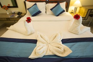 A neatly made bed with towels arranged in a decorative pattern, a bedside table with a lamp, and a nightstand with a vase of flowers. - Hotel Mint Highstreet (Pune)